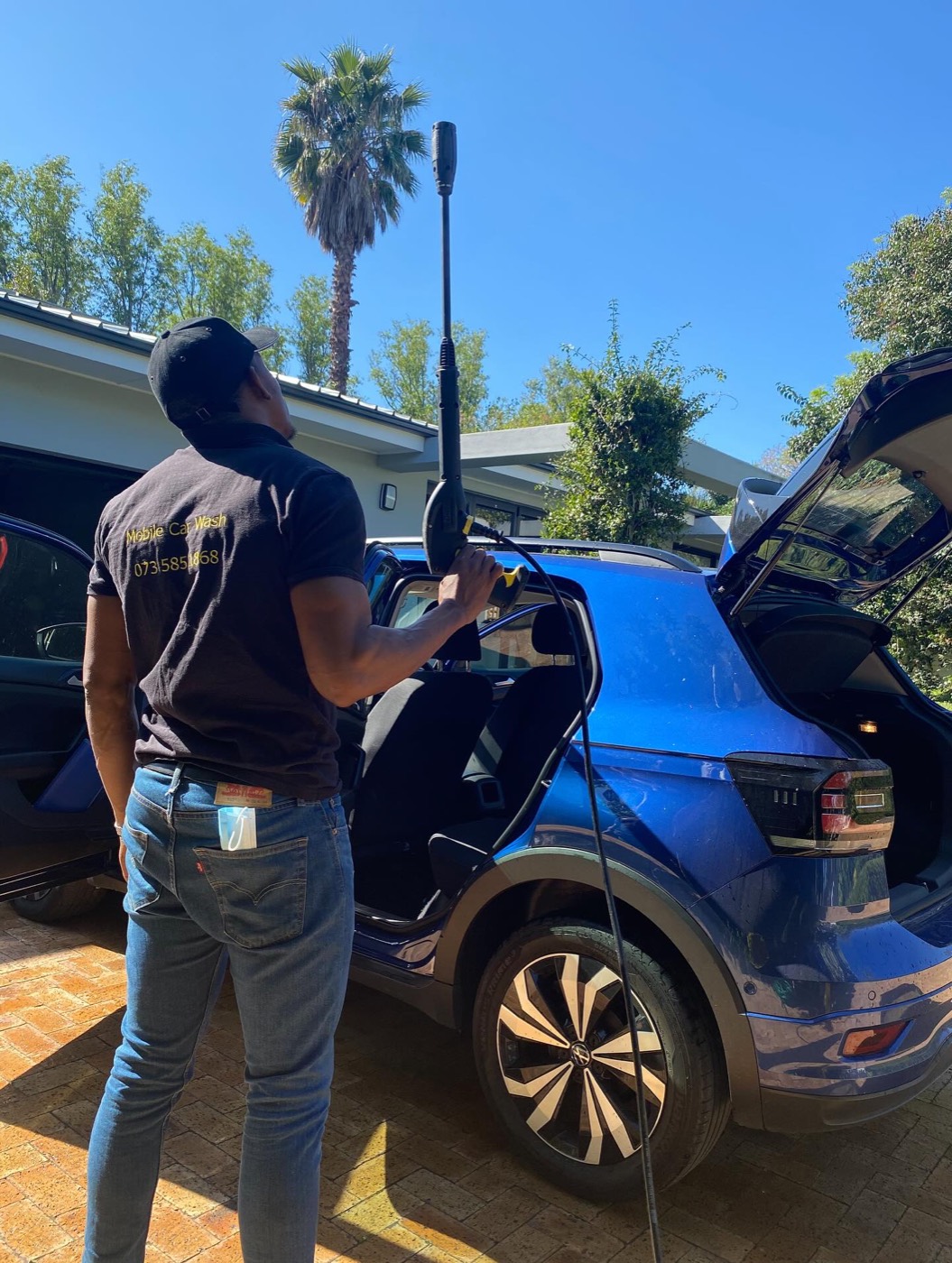 Hydrofit Mobile Car Wash team member in branded uniform pressure washing a blue VW T-Cross in Somerset West